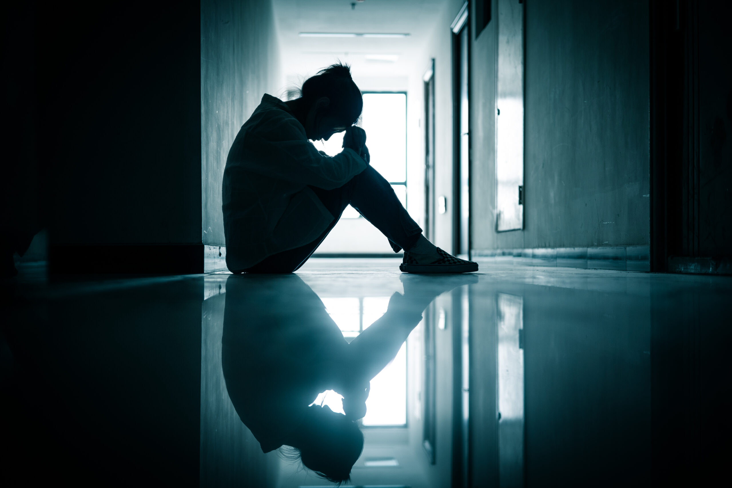 woman sitting in a hallway with her hands on her head, displaying signs of dizziness, vertigo, and nausea.