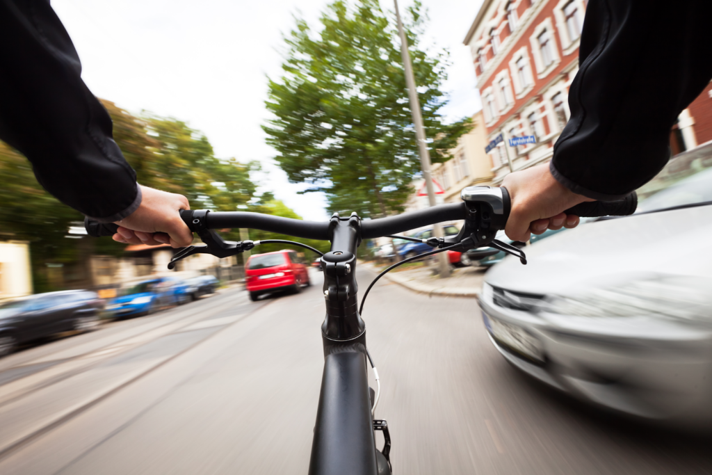 bicyclist riding on a street with a car coming out into their path at an intersection. 