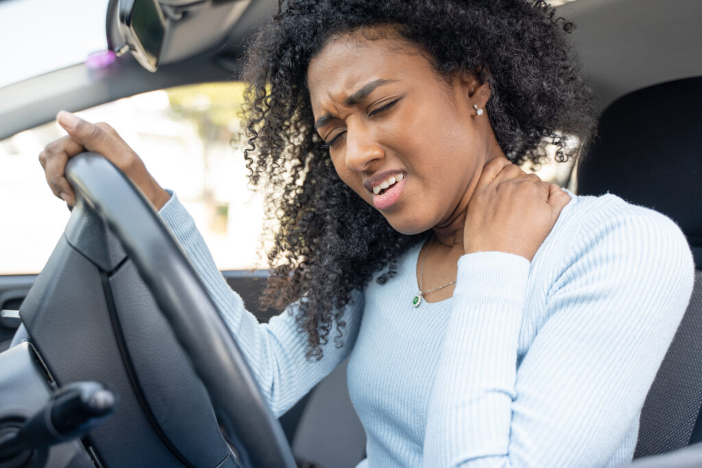 A woman grabs her neck and scowls in pain after a car accident.