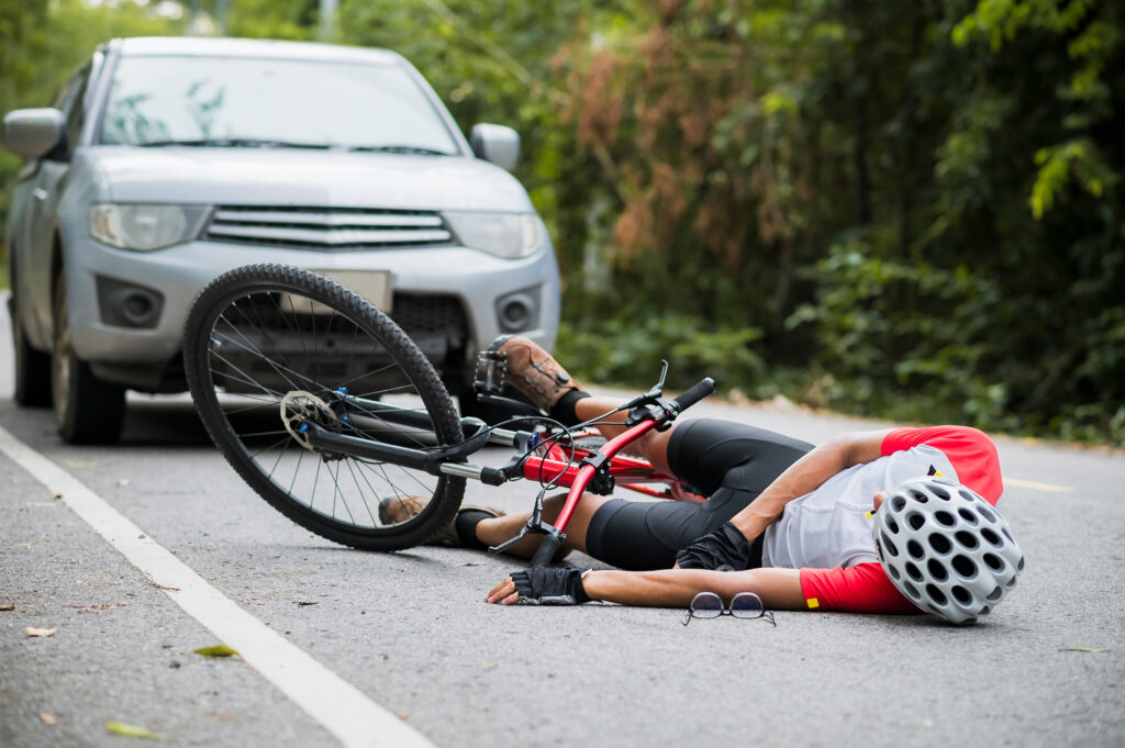 A man lies on the ground injured after being hit by a car while riding his bicycle. 